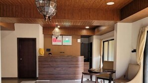 A reception area with a wooden ceiling, a reception desk, a seating area with a table and chairs, and a check-in counter. - Mastiff Grand La Villae Resort, Lonavala (Mawal)