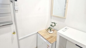 Ein kleiner, sauberer Raum mit einer weißen Wand, einer Holztheke, einem kleinen Kühlschrank, einem Spiegel und einer Klimaanlage.