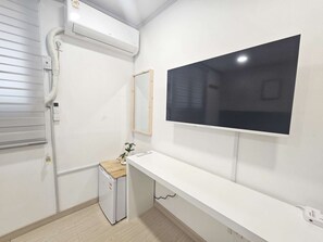 A small, clean room with a white wall, a mounted TV, a small fridge, and a wooden cabinet.