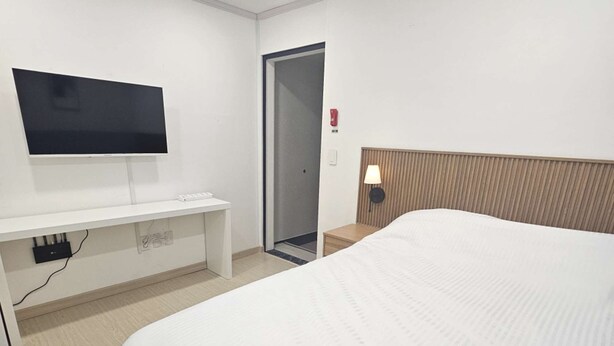 Ein Hotelzimmer mit Bett, Wandfernseher, Nachttisch und Tür.