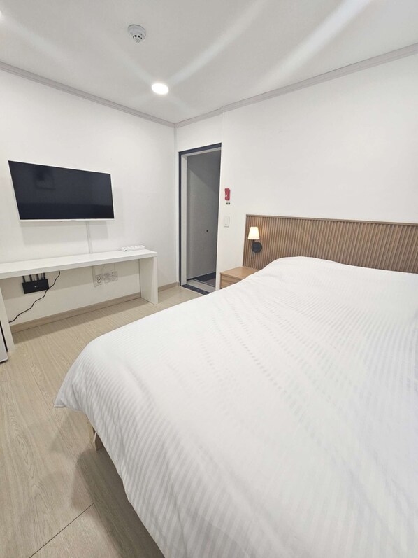 A hotel room with a bed, a TV mounted on the wall, a bedside table, and a door.