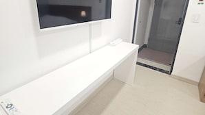Ein modernes Hotelzimmer mit einem an der Wand montierten Flachbildfernseher, einem weißen Konsolentisch und einer Tür, die zu einem Flur führt.