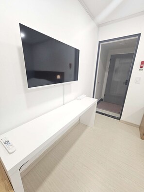 Et moderne hotelværelse med et fladskærms-tv ophængt på væggen, et hvidt konsolbord og en dør, der fører til en gang.