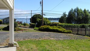 A residential area with a house, a gravel driveway, a wooden fence, and a view of a body of water.