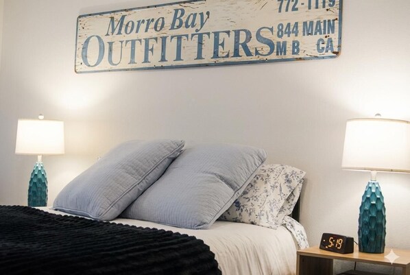 A bedroom with a bed, two bedside lamps, a wall clock, and a sign above the bed.