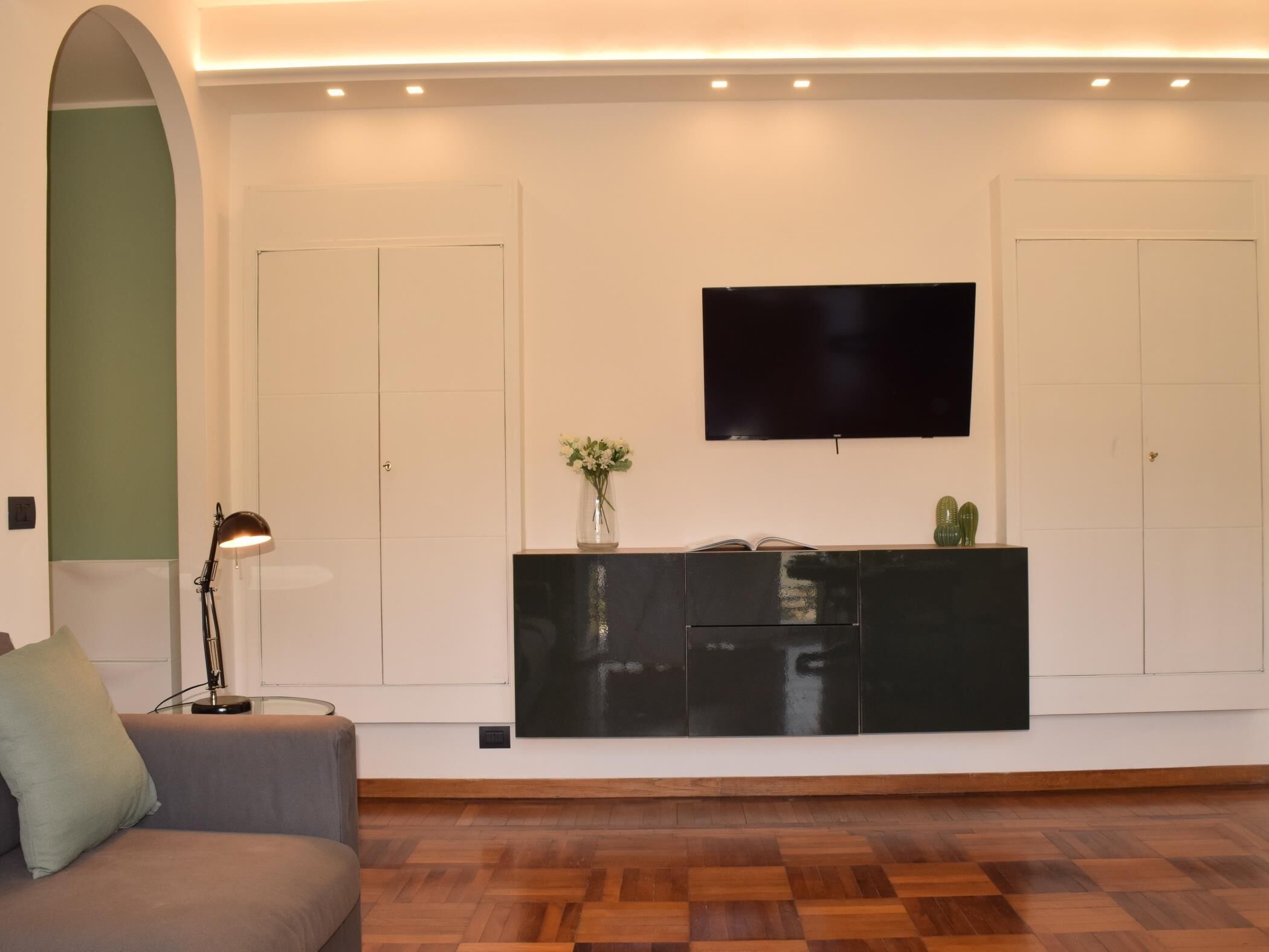 Ein modernes Wohnzimmer mit einer Couch, einer schwarzen Unterhaltungseinheit, einem Flachbildfernseher und Holzboden.