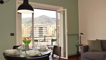 Ein Essbereich mit Tisch für vier Personen, einer Couch und Blick auf Gebäude und Berge durch eine Glastür.