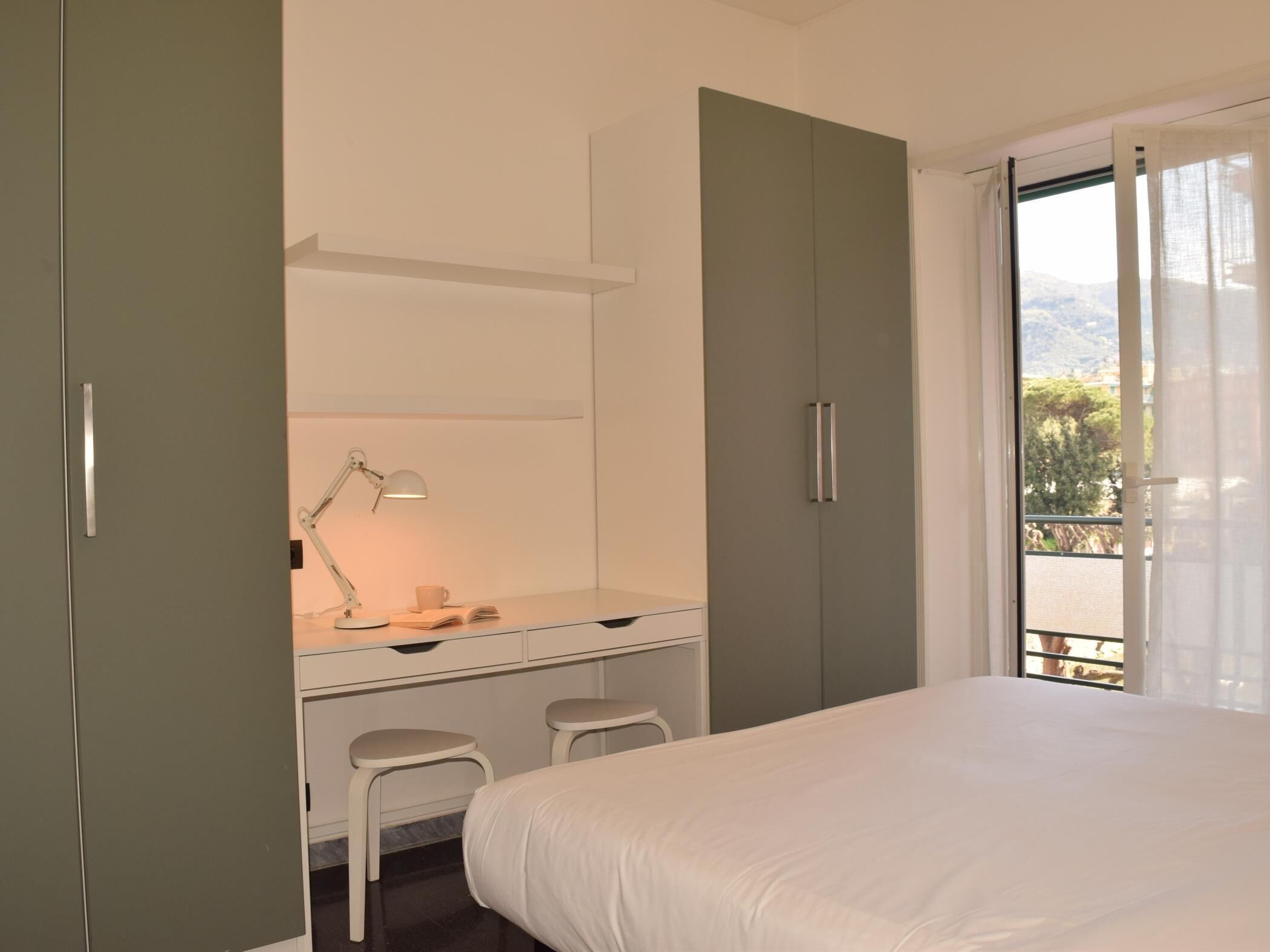 Ein Schlafzimmer mit einem Bett, einem Schreibtisch mit Stuhl und einem Fenster mit Blick ins Freie.