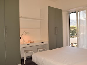 Ein Schlafzimmer mit einem Bett, einem Schreibtisch mit Stuhl und einem Fenster mit Blick ins Freie.