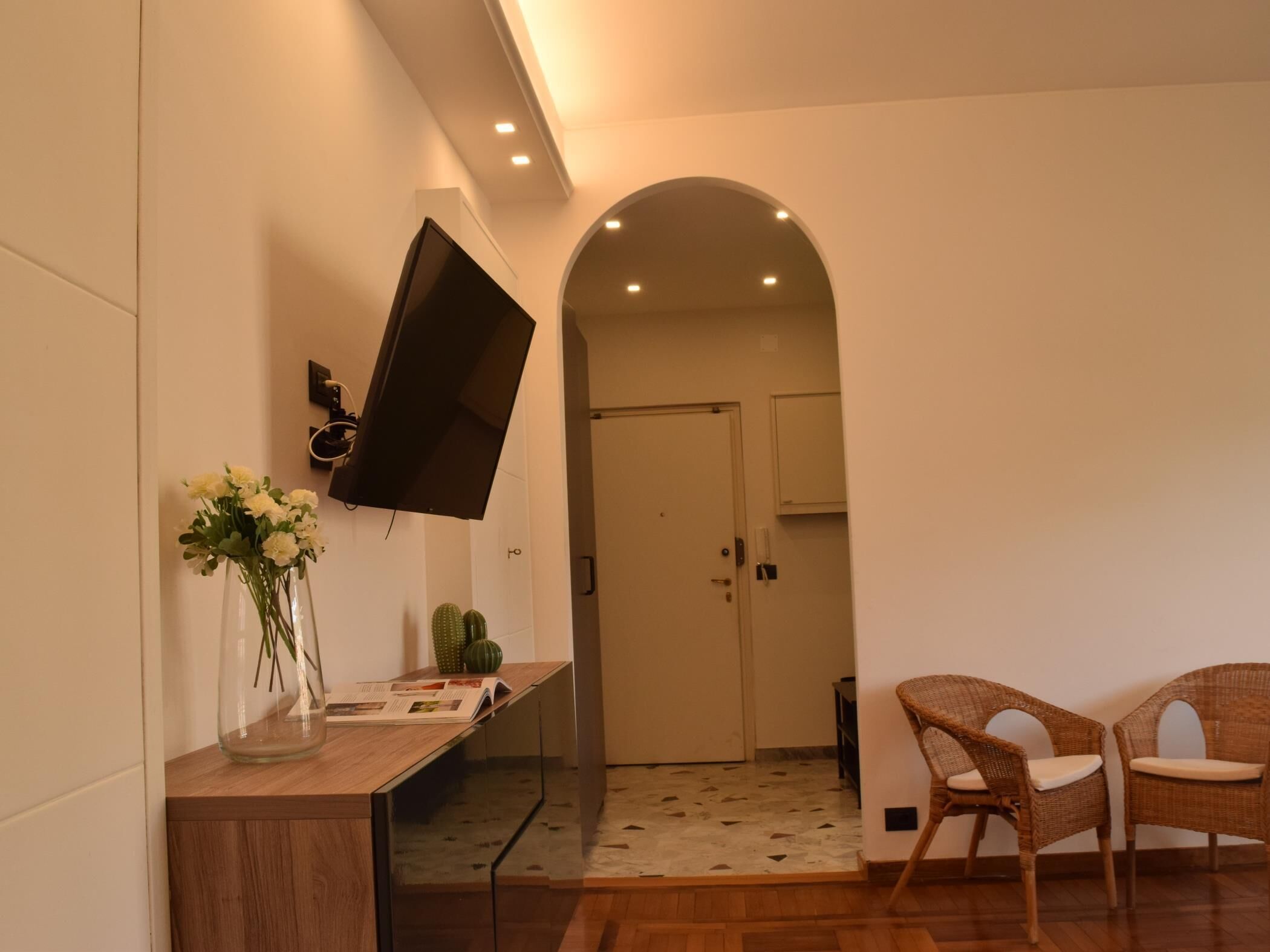 Ein modernes Interieur mit einem wandmontierten Flachbildfernseher, einem Holztischchen mit Blumenvase und Korbstühlen.