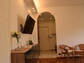 Ein modernes Interieur mit einem wandmontierten Flachbildfernseher, einem Holztischchen mit Blumenvase und Korbstühlen.