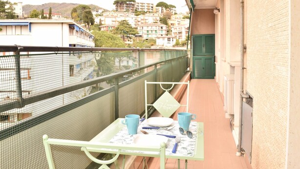 Ein Balkon mit Tisch für zwei Personen, einem Stuhl und Blick auf Geb äude und Hügel im Hintergrund.