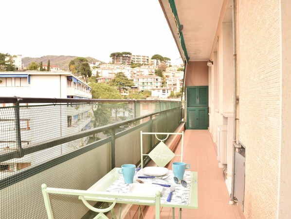 A balcony with a table set for two, a chair, and a view of buildings and hills in the background. - Rental unit in Rapallo - 2 bedrooms 1 bathroom air conditioned (RAPALLO)