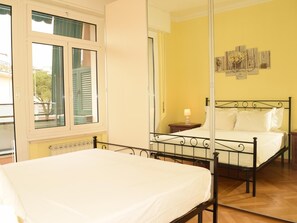 A bedroom with a bed, a nightstand, a mirror, and a window with shutters. - Rental unit in Rapallo - 2 bedrooms 1 bathroom air conditioned (RAPALLO)
