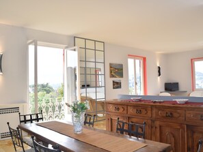 Ein Essbereich mit einem Holztisch, Stühlen, einer Blumenvase, einem Fernseher und einem Balkon mit Aussicht.