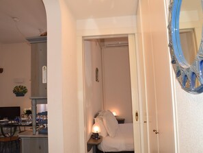 Ein Zimmer mit einem Bett, einem Nachttisch mit Lampe, einem Spiegel und einem Schreibtisch mit Stuhl.