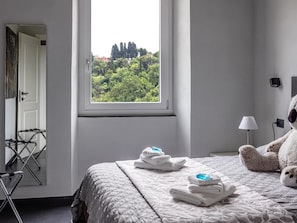 Ein Schlafzimmer mit einem Bett, einem Fenster mit Blick auf Bäume, einer Lampe und einem Stofftier.