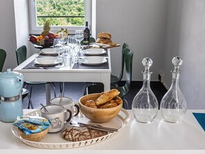Ein Esstisch ist gedeckt mit Tellern, Gläsern, einer Flasche, einer Schüssel mit Croissants, einer Kaffeetasse und einem Teekännchen.