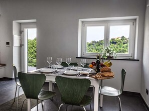 Ein Essbereich mit einem Tisch für vier Personen, Stühlen, einem Fenster mit Blick auf Grünflächen und einem Obstkorb auf dem Tisch.
