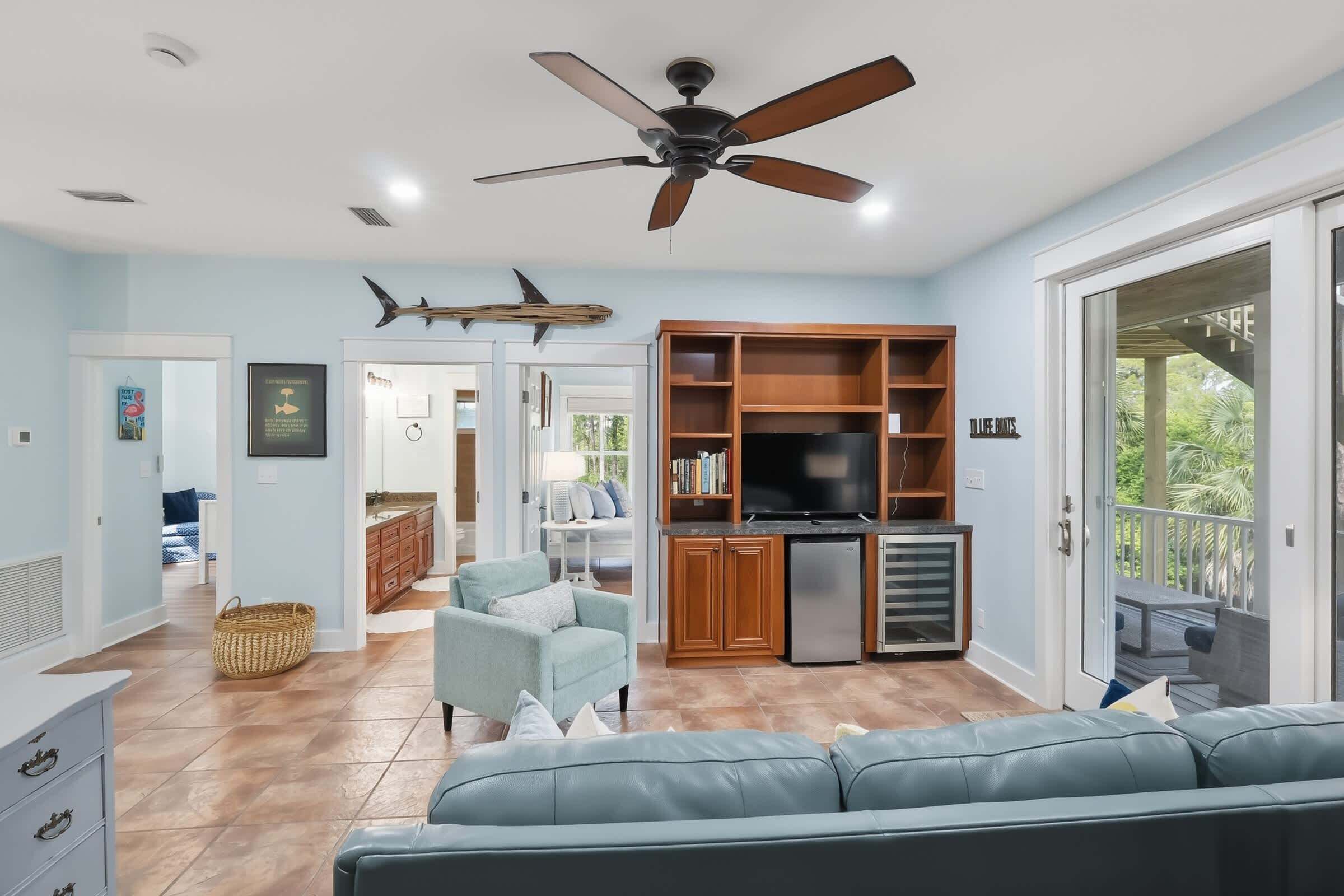 A living room with a ceiling fan, a TV, a bookshelf, and a dining area with a table and chairs.