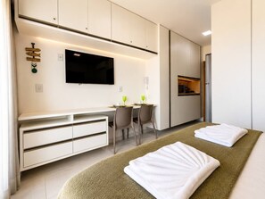 Quarto de hotel moderno com cama, escrivaninha, cadeira, televisão e minibar.