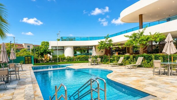 Una piscina con escalones, sillas de descanso y un edificio moderno al fondo.