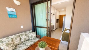 Una habitación con un sofá, una mesa de madera con una planta, un cartel en la pared y una puerta corredera que da al baño.