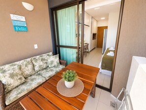 Una habitación con un sofá, una mesa de madera con una planta, un cartel en la pared y una puerta corredera que da al baño.