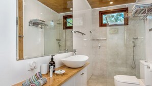 A modern bathroom with a large white sink, a wooden vanity, a glass shower enclosure, and a toilet.