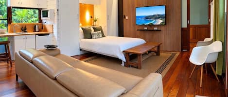 A compact room with a bed, a sofa, a TV, and a kitchenette.