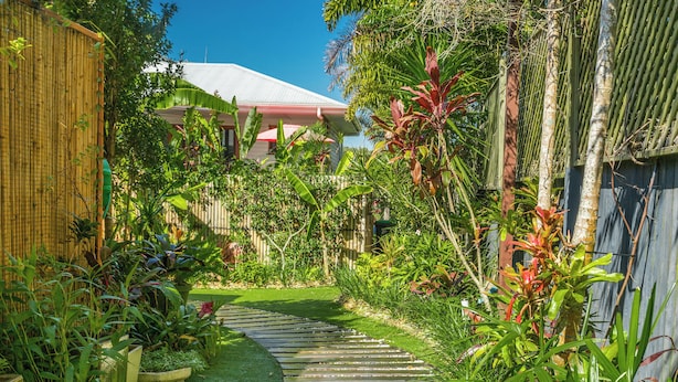 A garden with a curved pathway, lush greenery, and a building with a white roof.
