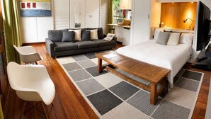 A modern hotel room with a bed, sofa, dining area, and a view of the outdoors.