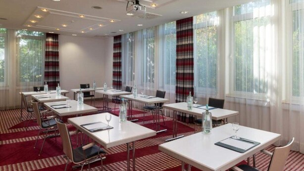Un salón de conferencias con mesas y sillas blancas, y un proyector.