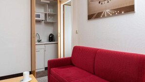 Una habitación con un sofá rojo, una mesa de comedor con una taza, una zona de cocina con armarios y un microondas, y un cuadro colgado en la pared con un avión.