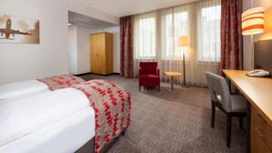 Una habitación de hotel con cama, escritorio, silla, armario y lámpara.