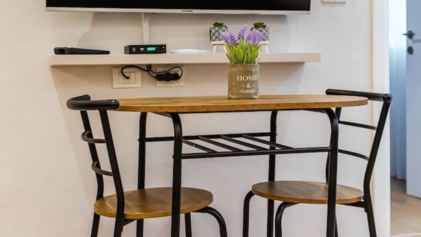 A modern living room with a flat-screen TV mounted on the wall, a small table with two chairs, and a decorative vase on the table. - Stone City Stay Central Gjirokast r Apartment (Gjirokastër)