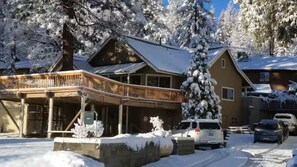 Eine Lodge mit einer Holzterrasse, schneebedeckten Bäumen und einem geparkten Auto davor.