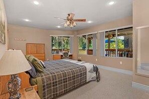 Ein Schlafzimmer mit einem Bett, einem Schreibtisch, einem Stuhl, einem Deckenventilator und großen Fenstern.