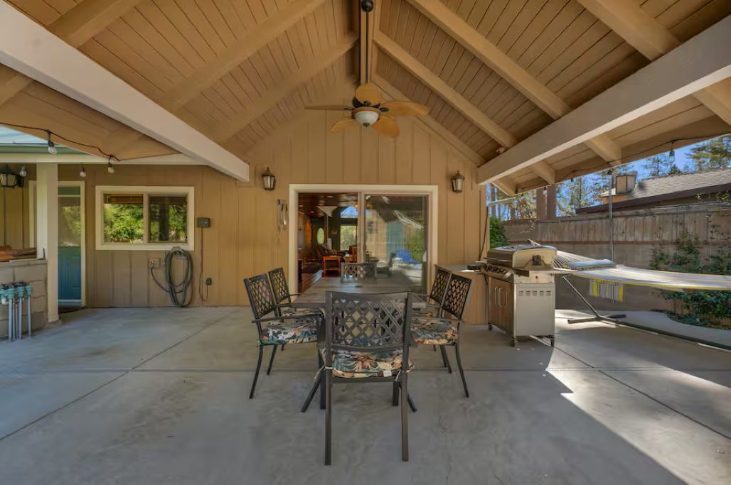 A covered patio area with a dining table and chairs, a ceiling fan, and a grill.