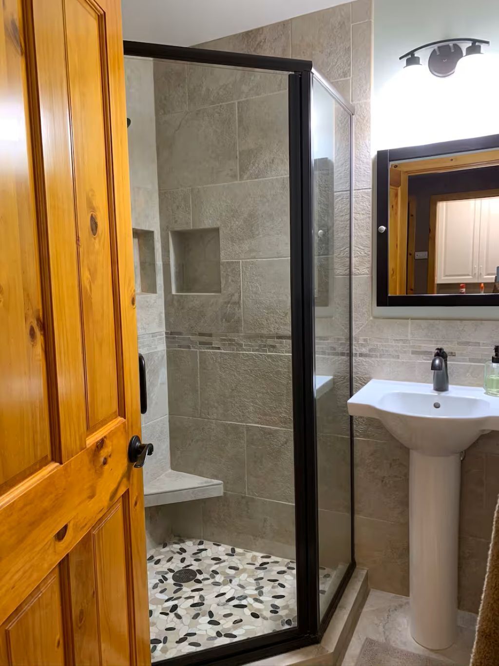 A bathroom with a glass shower enclosure, a pedestal sink, and a wooden door.