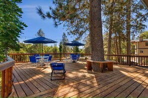 Eine Holzterrasse mit blauen Stühlen und Sonnenschirmen, umgeben von Bäumen.