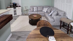 A living room with a sectional sofa, a round coffee table, a wooden dining table, and a ceiling fan. - Quiet Neighborhood walking by eagle creek close to downtown and speedway (Indianapolis)