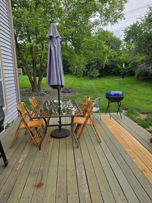 A wooden deck with a table and chairs, a barbecue grill, and a covered umbrella.