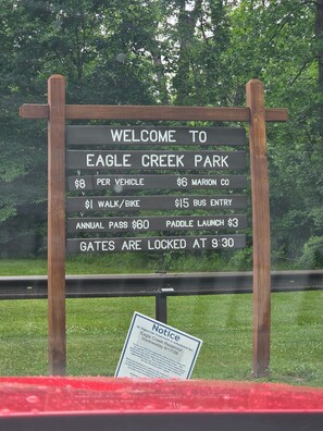 Letrero de bienvenida en el Parque Eagle Creek que indica tarifas de estacionamiento, un aviso sobre tratamiento de algas y un aviso sobre el cierre de las puertas a las 9:30.