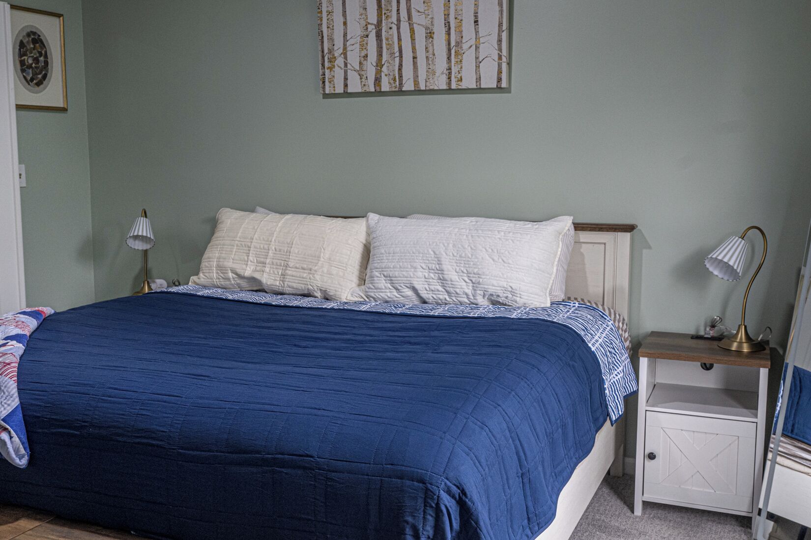 Een slaapkamer met een bed, twee nachtkastjes, een lamp en een kunstwerk aan de muur.