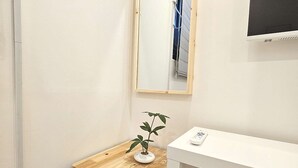 Eine kompakte Küchenzeile mit kleinem Kühlschrank, einer Holzausziehtafel, einem Topf mit Pflanze, einem Spiegel und einem weißen Schreibtisch.