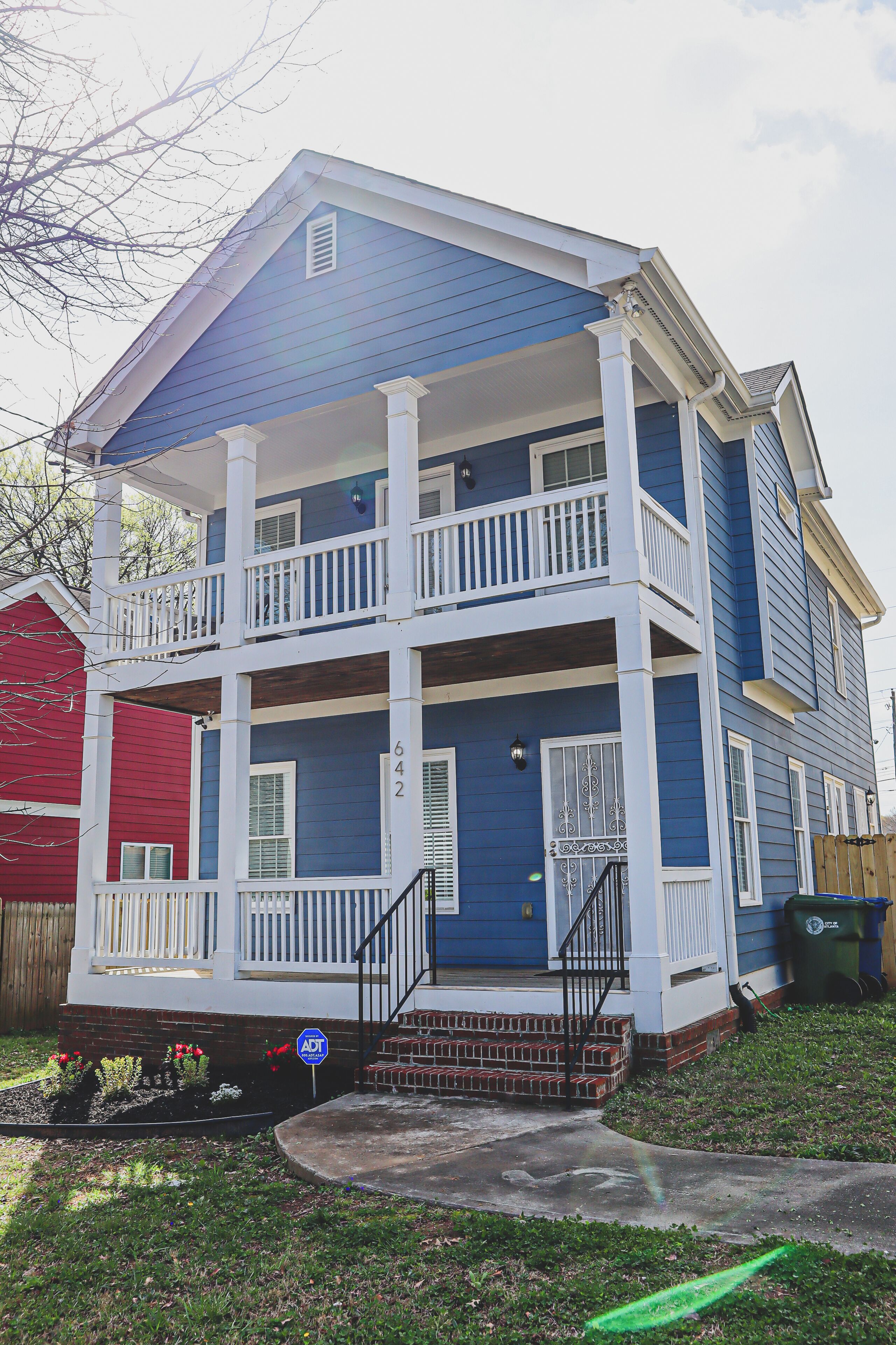 A two-story building with a balcony on the second floor, a front porch, and a brick foundation.
