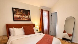 Een slaapkamer met een bed, een plafondventilator, een nachtkastje, een lamp, een schilderij, een spiegel en een deur.