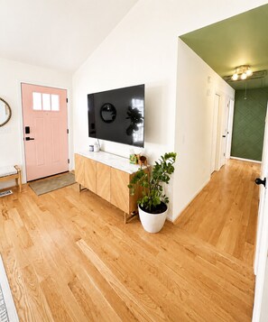 Ein Flur mit Holzboden, einer weißen Tür, einem an der Wand montierten Fernseher, einem Blumentopf und einer grünen Wand.