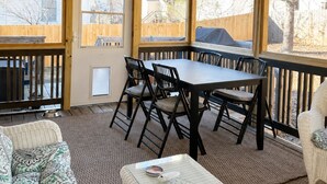 Een overdekt terras met een tafel en stoelen, een rieten bank en een plafondventilator.